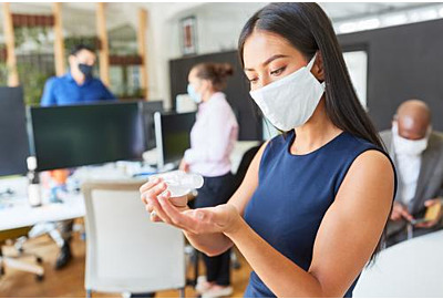 Geschäftsfrau mit Gesichtsmaske im Büro, das die Hände desinfiziert, wegen Covid-19 und Corona-Virus